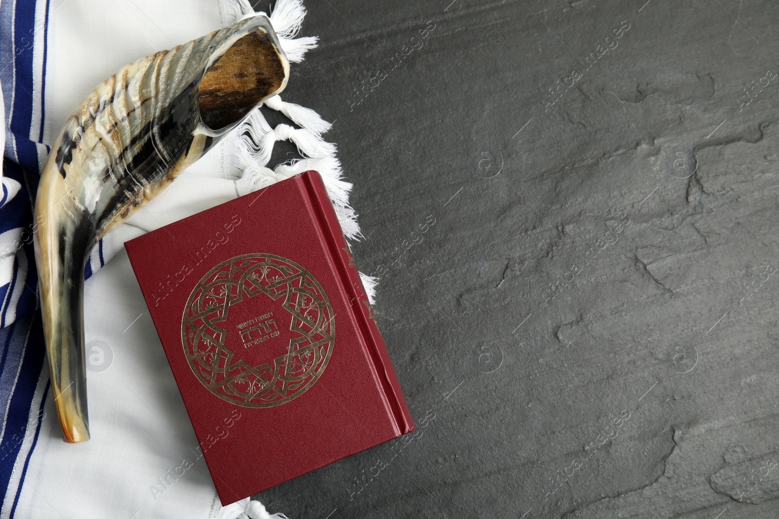 Photo of Tallit, shofar and Torah on black slate table, flat lay with space for text. Rosh Hashanah celebration