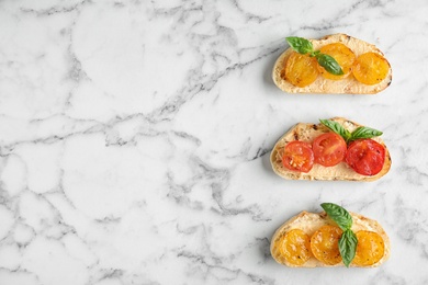 Photo of Delicious tomato bruschettas on white marble background, flat lay. Space for text