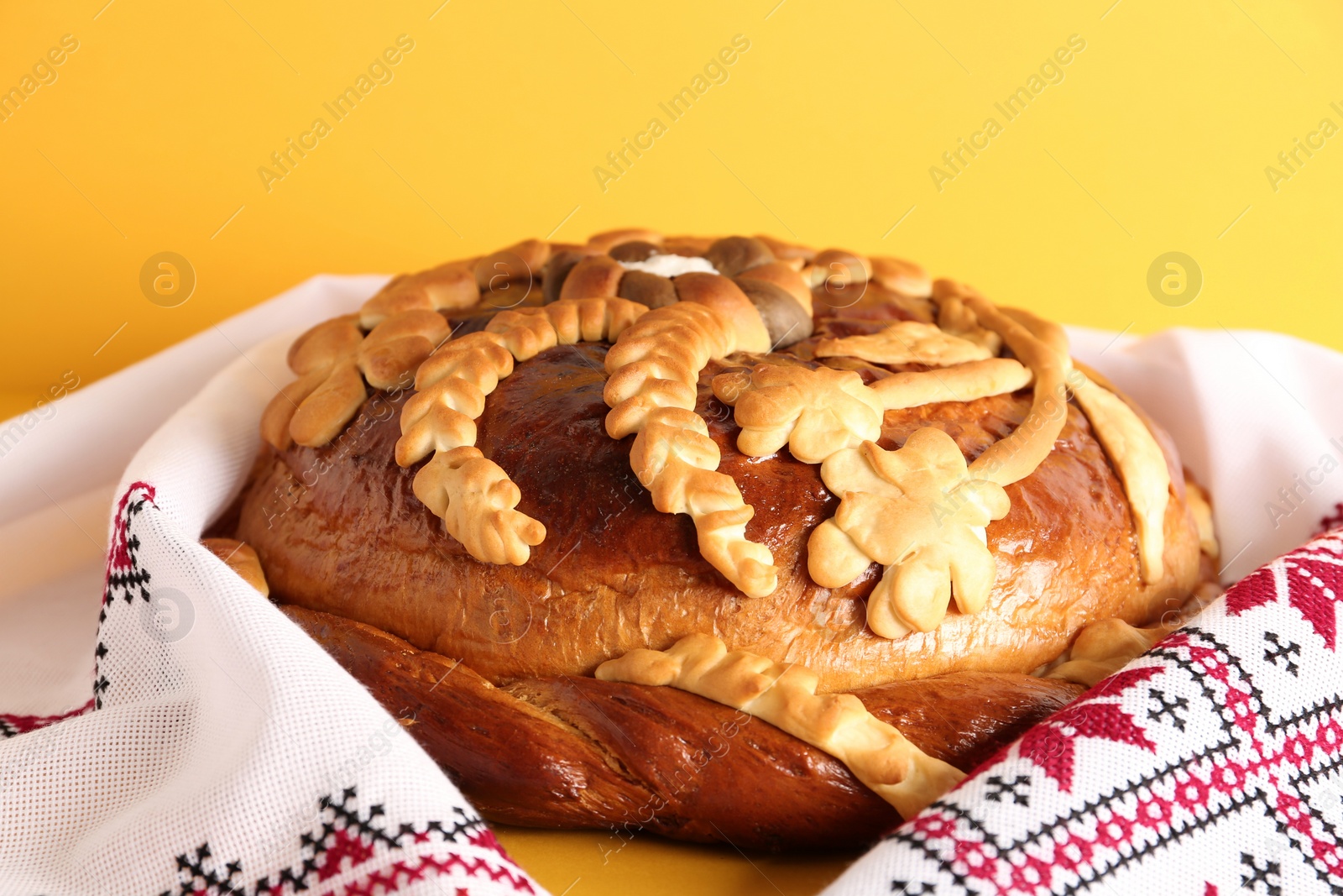 Photo of Rushnyk with korovai on yellow background, closeup. Ukrainian bread and salt welcoming tradition