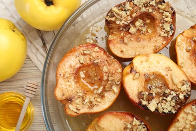 Delicious baked quinces with nuts in bowl, honey and fresh fruits on wooden table, flat lay