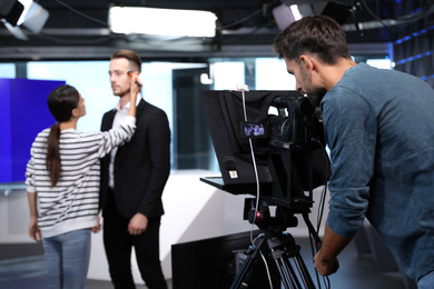 Photo of Presenter, makeup artist and video camera operator working in studio. News broadcasting