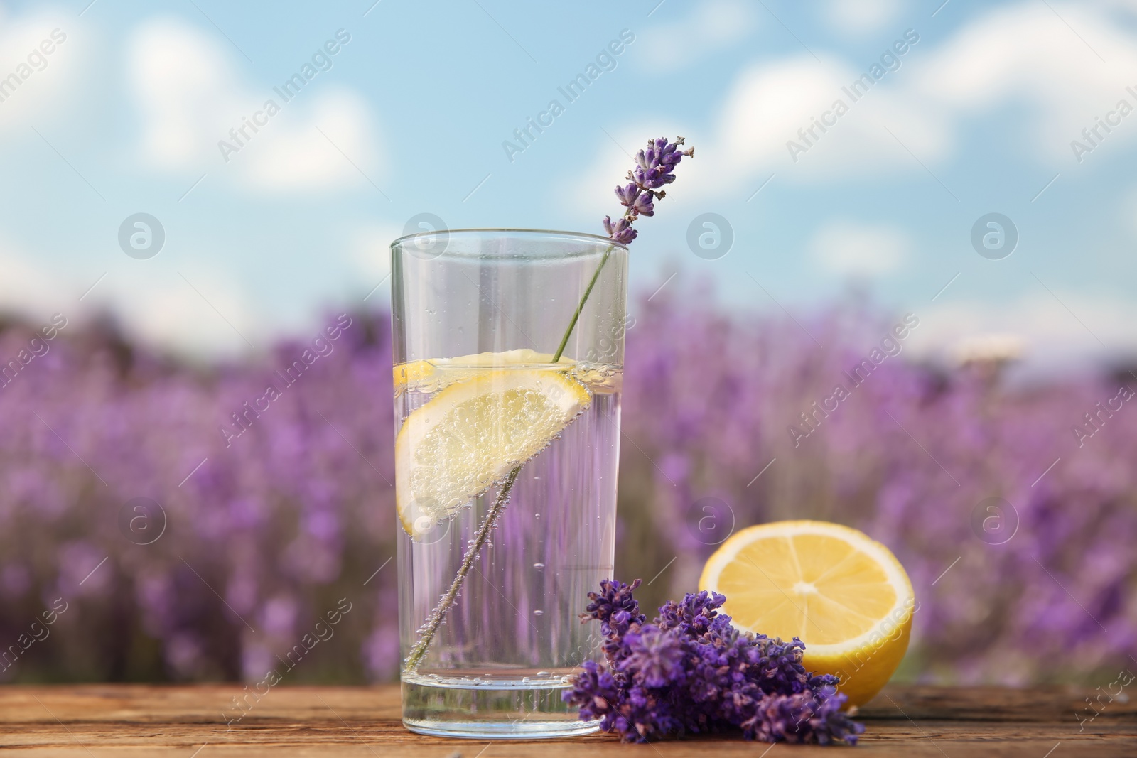 Photo of Lemonade with lemon slices and lavender flowers on wooden table outdoors, closeup