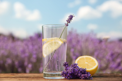 Photo of Lemonade with lemon slices and lavender flowers on wooden table outdoors, closeup