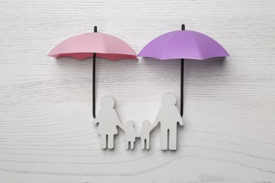 Photo of Small umbrellas and family figure on white wooden background, flat lay