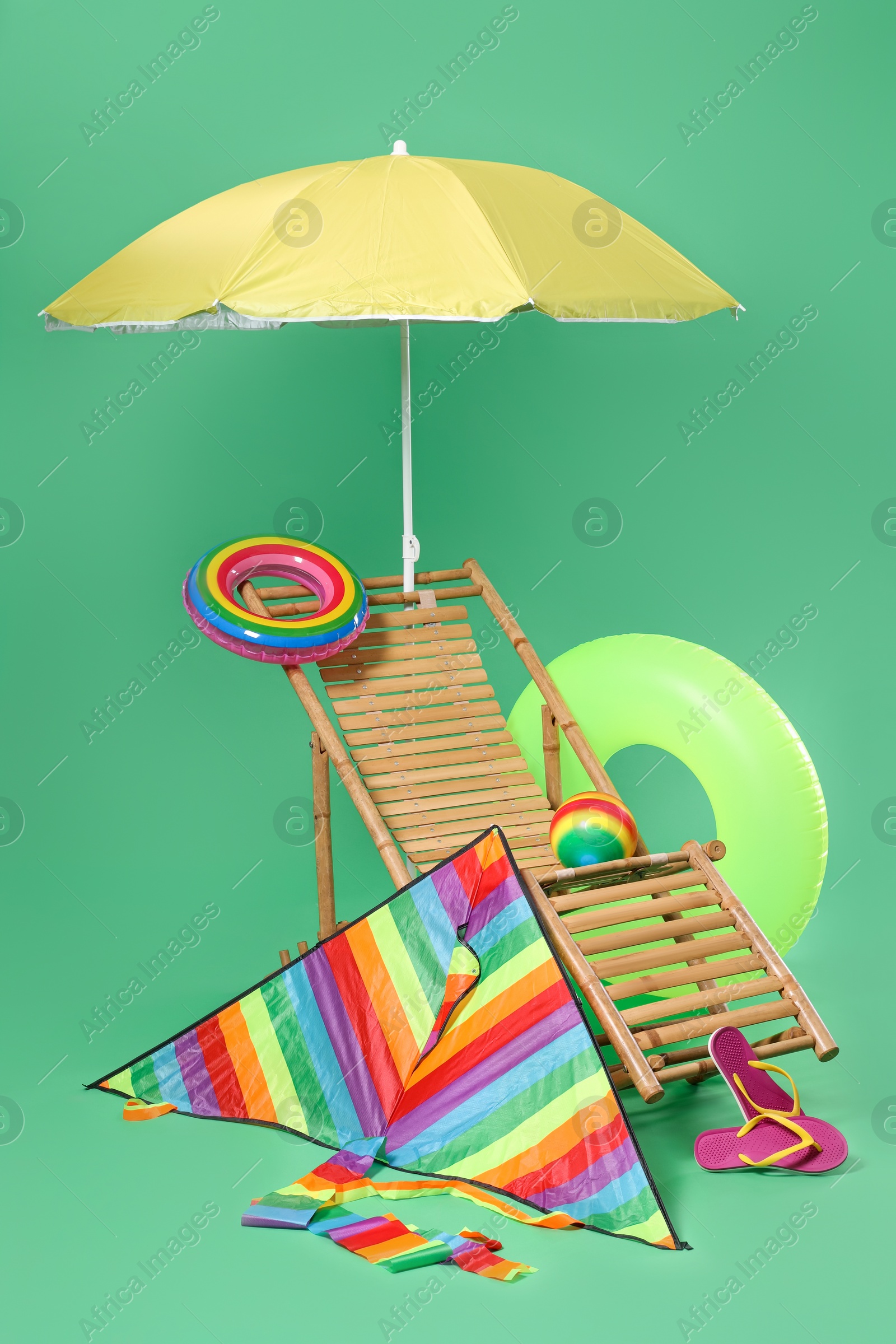 Deck chair, kite and beach accessories on green background Photo of Deck chair, kite and beach accessories on green background