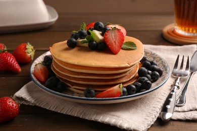 Photo of Delicious pancakes with fresh berries and butter served on wooden table, closeup