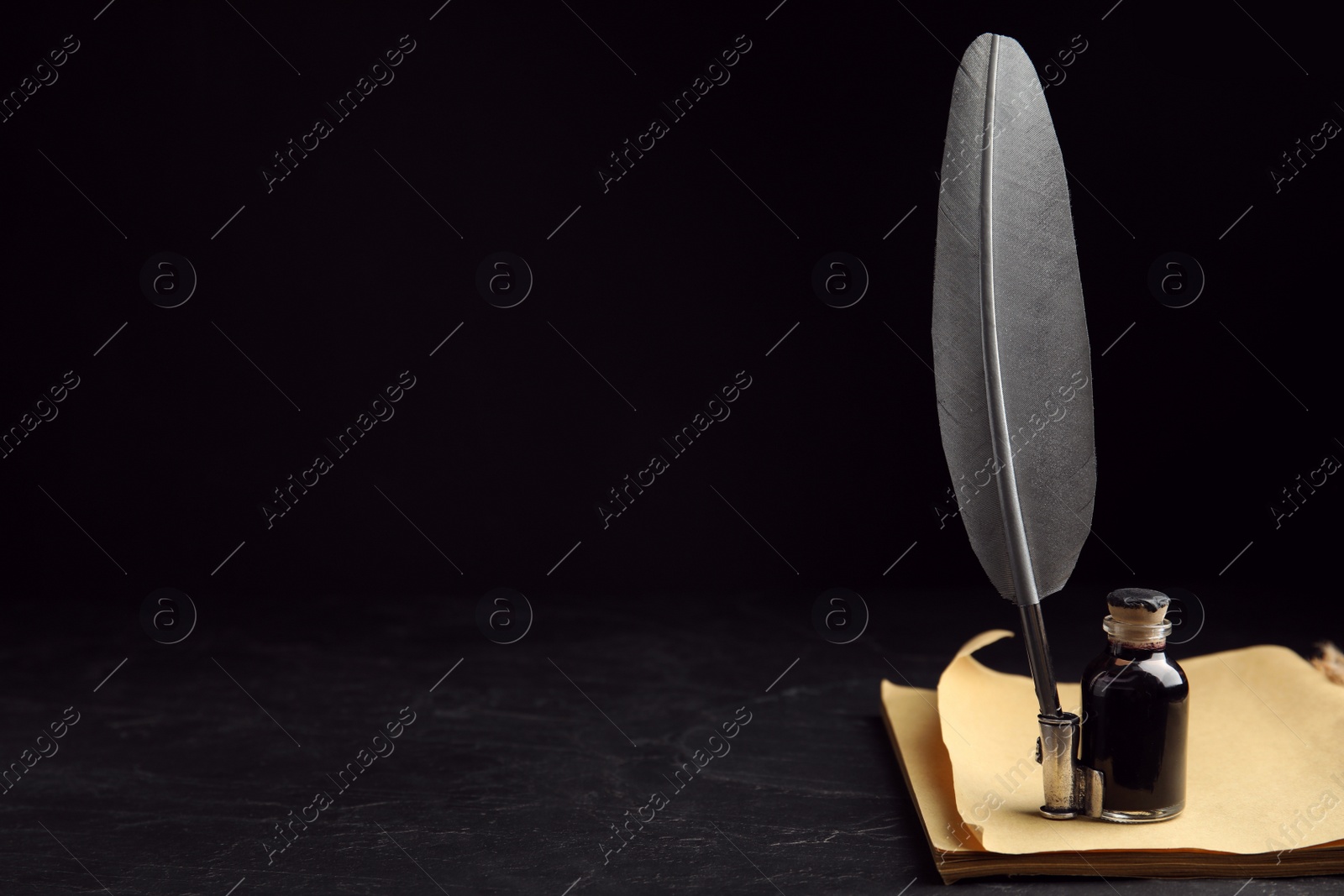 Photo of Feather pen, bottle of ink and old paper on black table. Space for text