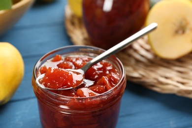 Photo of Delicious quince jam with spoon on blue table, closeup