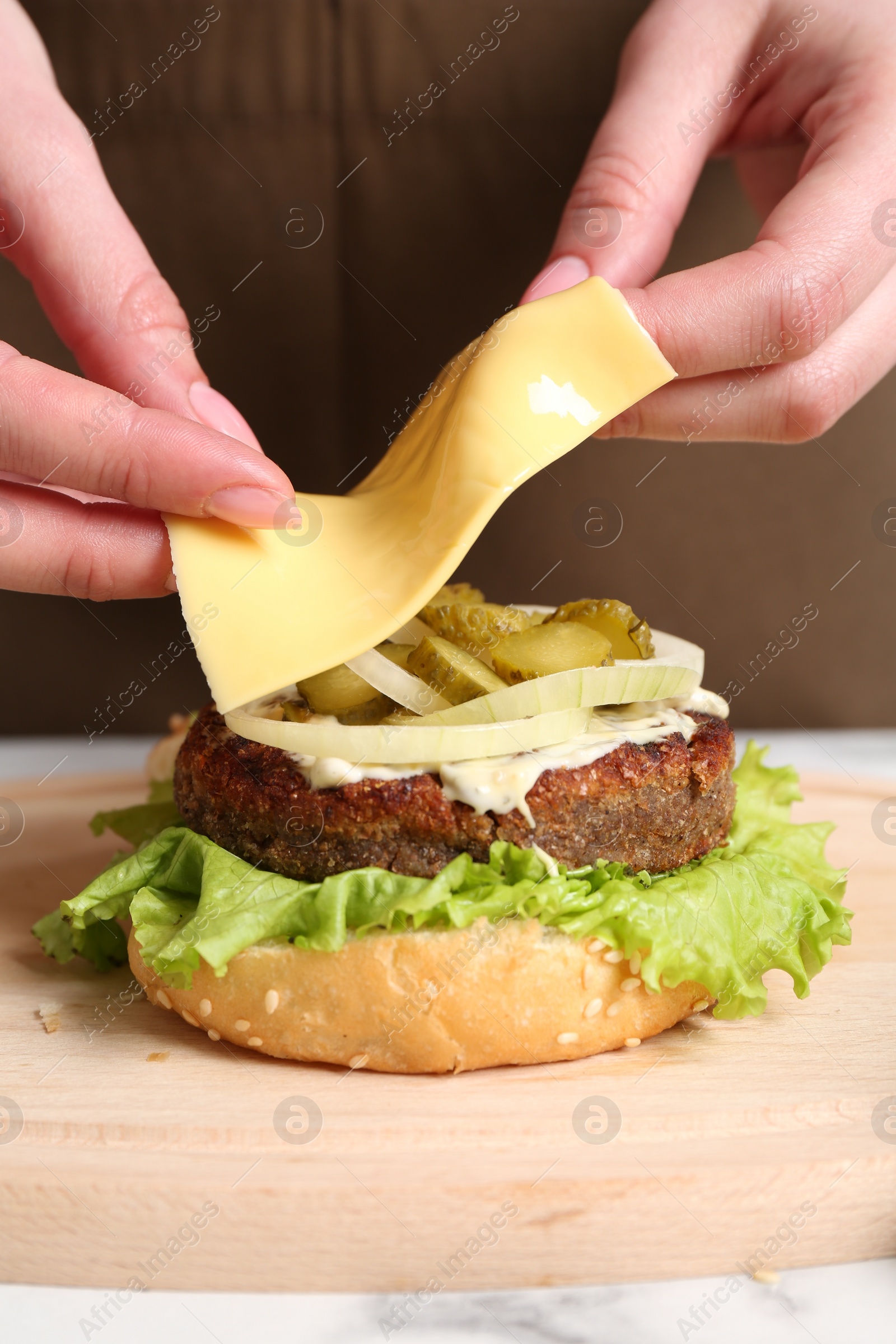 Photo of Woman making delicious vegetarian burger at table, closeup