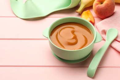 Photo of Bowl with tasty pureed baby food and ingredients on pink wooden table, space for text