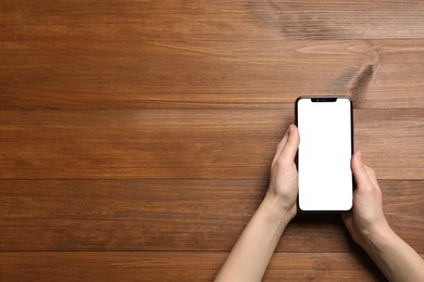 Woman with smartphone at wooden table, top view. Space for text