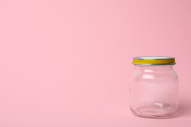 Closed empty glass jar on pink background, space for text