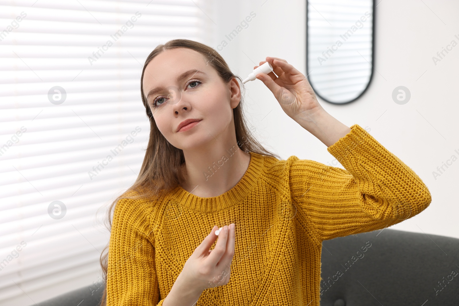 Photo of Young woman applying medical ear drops indoors