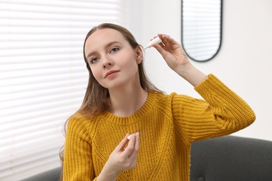 Young woman applying medical ear drops indoors