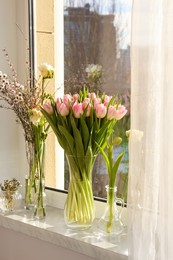 Photo of Many different spring flowers and branches with leaves on windowsill indoors