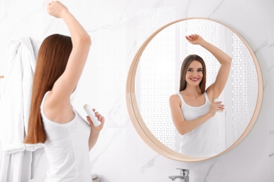 Photo of Beautiful young woman applying deodorant in bathroom