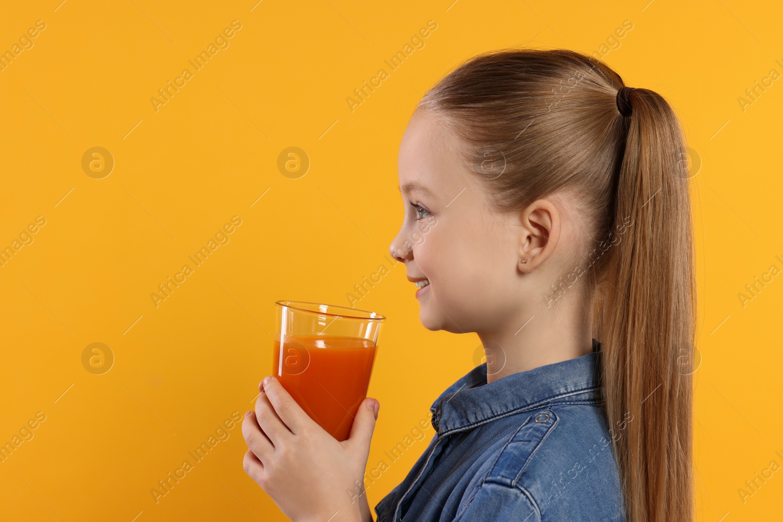 Photo of Cute little girl with glass of fresh juice on orange background, space for text