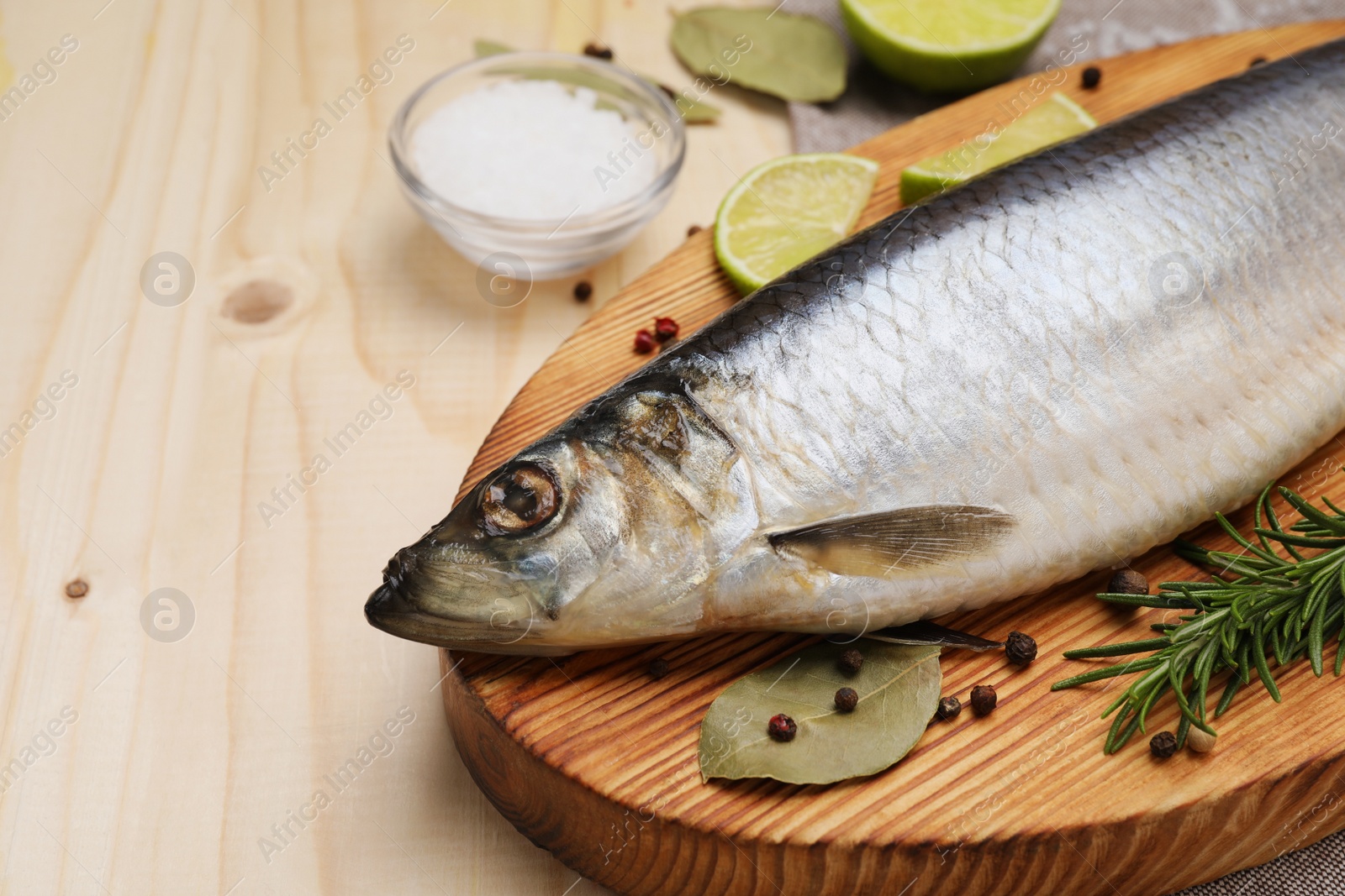 Photo of Delicious salted herring, bay leaves, lime, rosemary and salt on wooden table, closeup