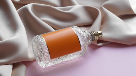 Photo of Luxurious bottle of perfume and beige silk on pink background