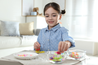 Photo of Little girl making accessory with beads at table indoors. Creative hobby