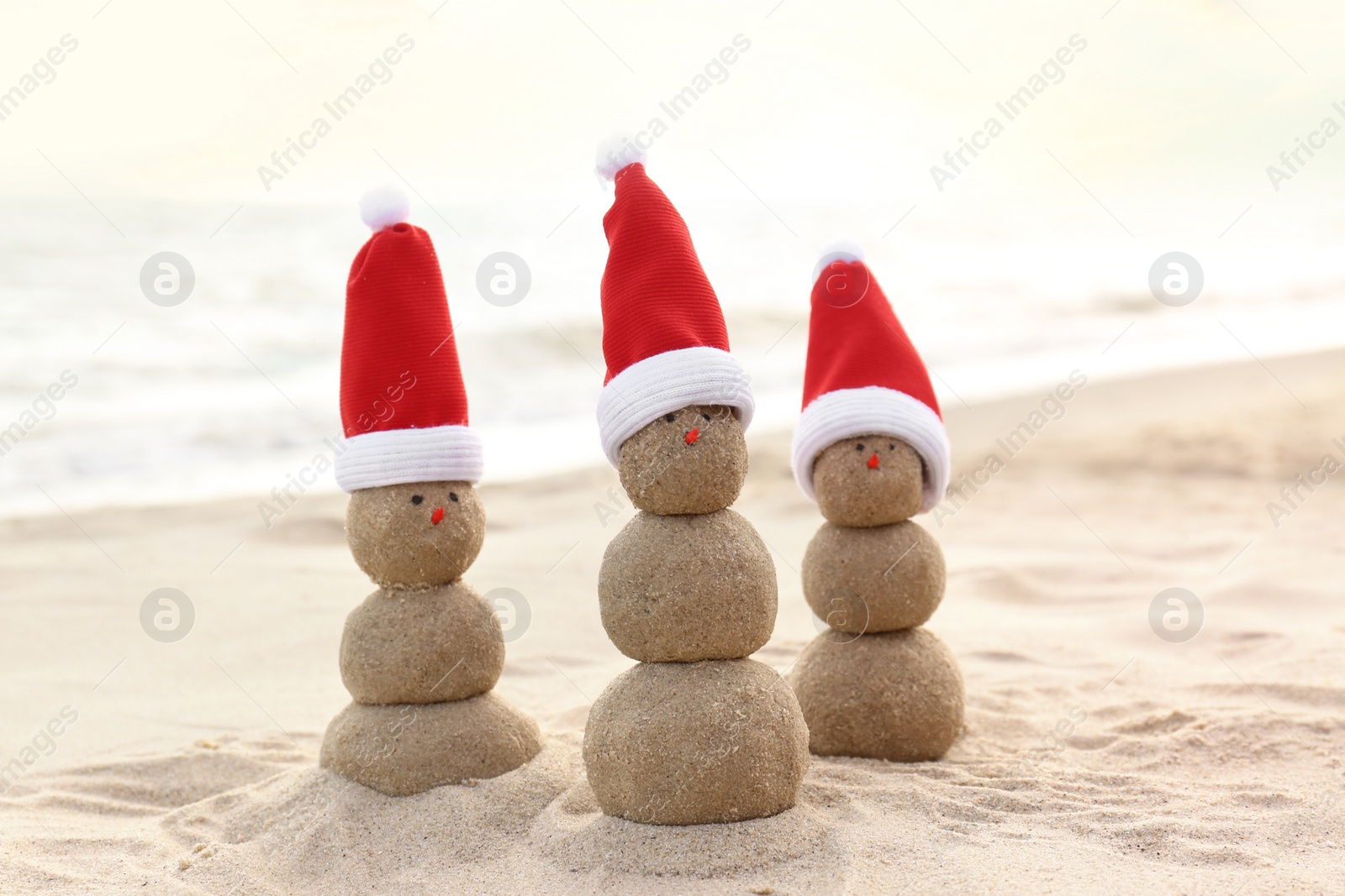 Photo of Snowmen made of sand with Santa hats on beach near sea. Christmas vacation