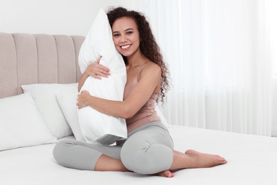 Photo of Happy African American woman hugging soft pillow on bed at home