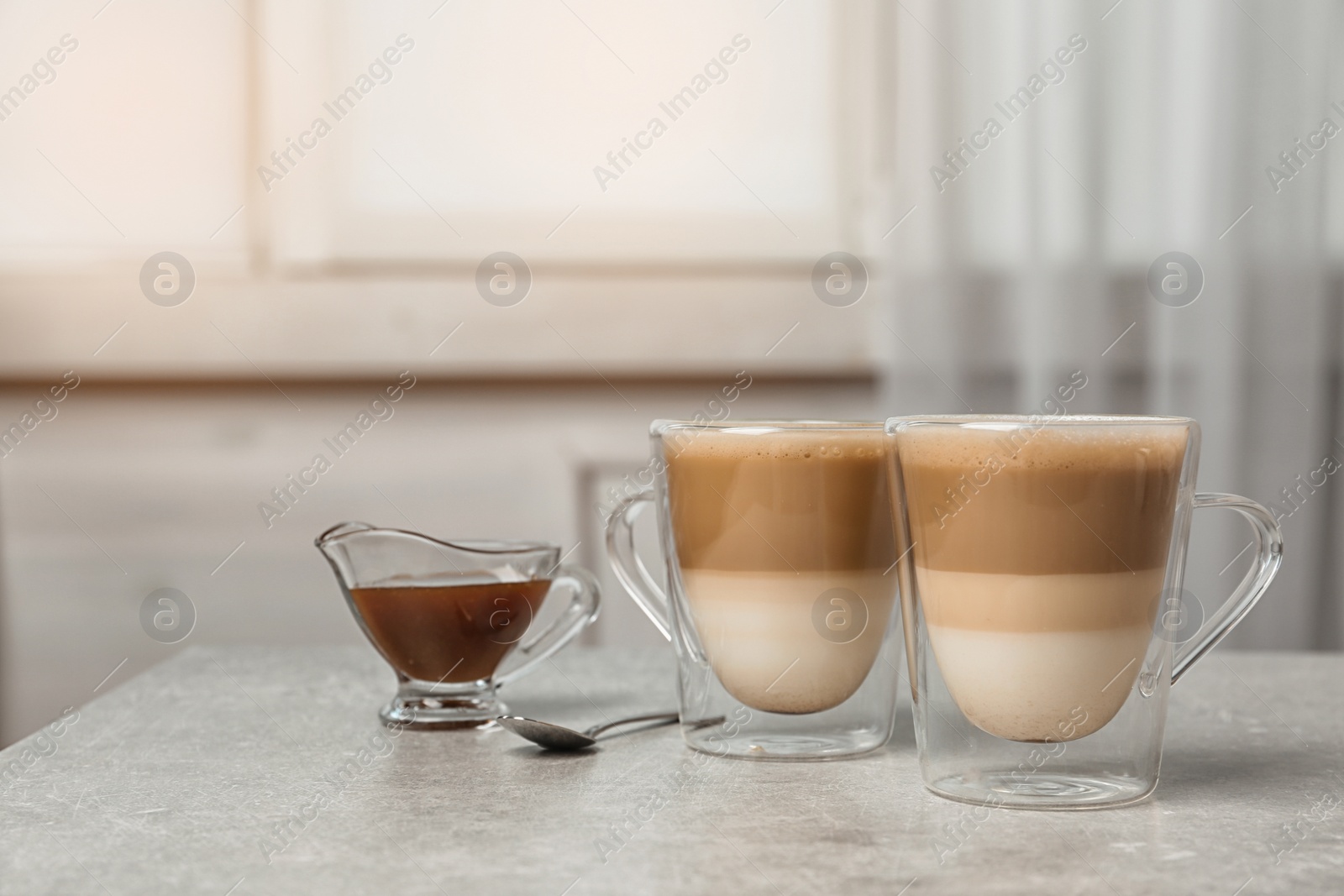 Photo of Glass cups of tasty caramel macchiato and gravy boat with syrup on table