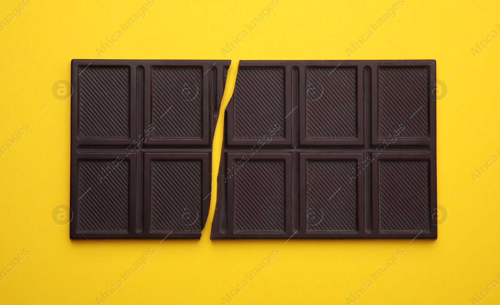 Photo of Broken chocolate bar on yellow background, top view