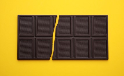 Photo of Broken chocolate bar on yellow background, top view