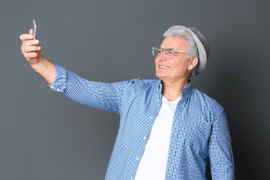 Mature man taking selfie against grey background