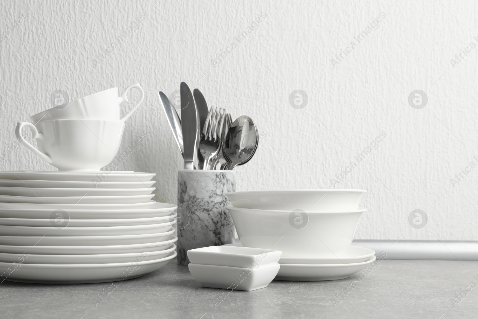 Photo of Set of clean dishes and cutlery on table near light wall. Space for text