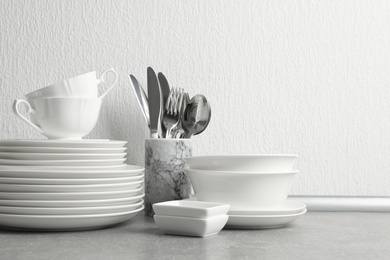 Photo of Set of clean dishes and cutlery on table near light wall. Space for text