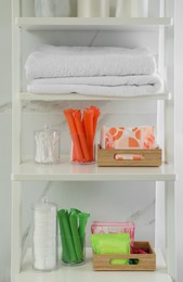 Photo of Towels, different feminine and personal care products on shelving unit in bathroom