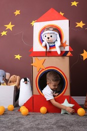 Photo of Cute little boy playing with cardboard rocket and toys at home. Child's room interior