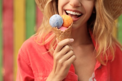 Happy young woman with delicious ice cream in waffle cone outdoors, closeup