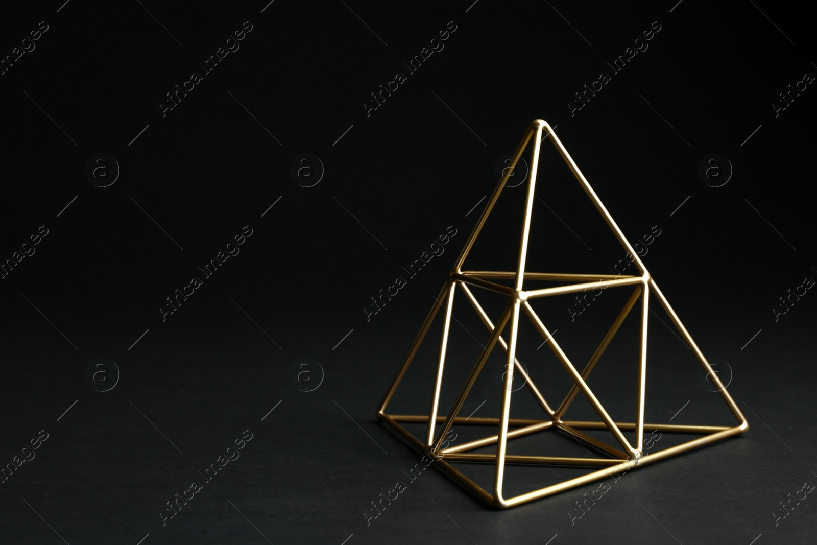 Photo of Shiny decorative gold pyramid on black background. Space for text
