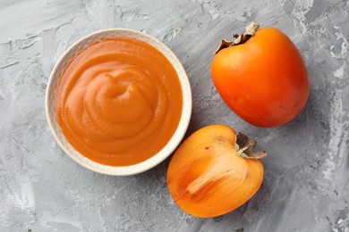 Delicious persimmon jam and fresh fruits on grey table, flat lay