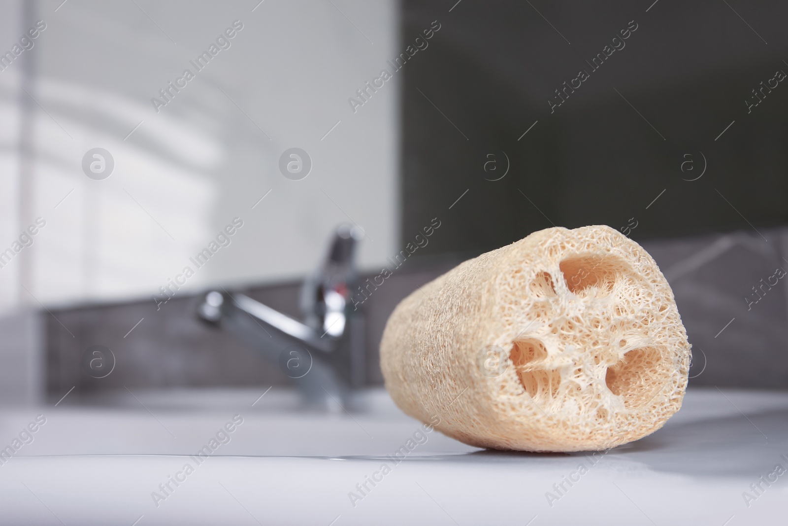 Photo of Natural loofah sponge on washbasin in bathroom, closeup. Space for text