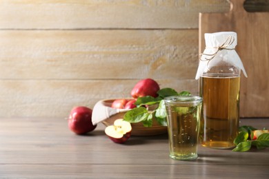 Photo of Delicious cider and apples with green leaves on wooden table, space for text