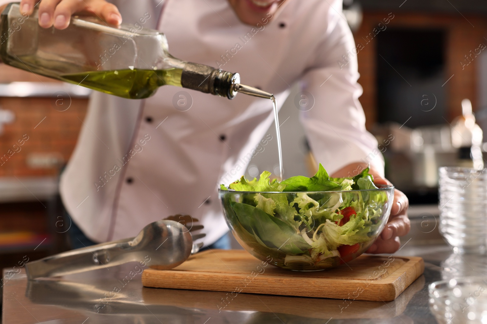 Photo of Professional chef pouring oil into bowl with fresh salad in restaurant kitchen, closeup