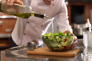 Photo of Professional chef pouring oil into bowl with fresh salad in restaurant kitchen, closeup