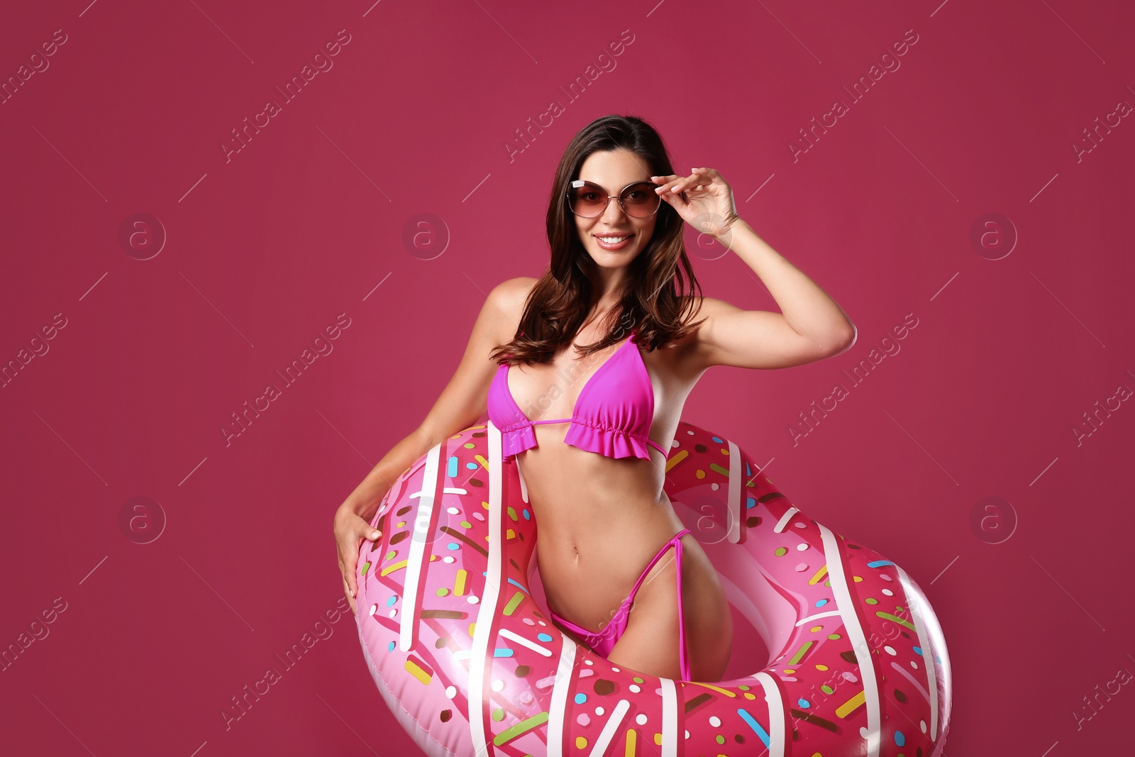 Photo of Beautiful woman in stylish bikini with inflatable ring on crimson background