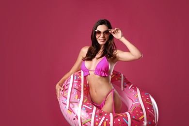 Beautiful woman in stylish bikini with inflatable ring on crimson background