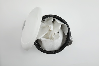 Trash bin with used toilet paper on white background, top view