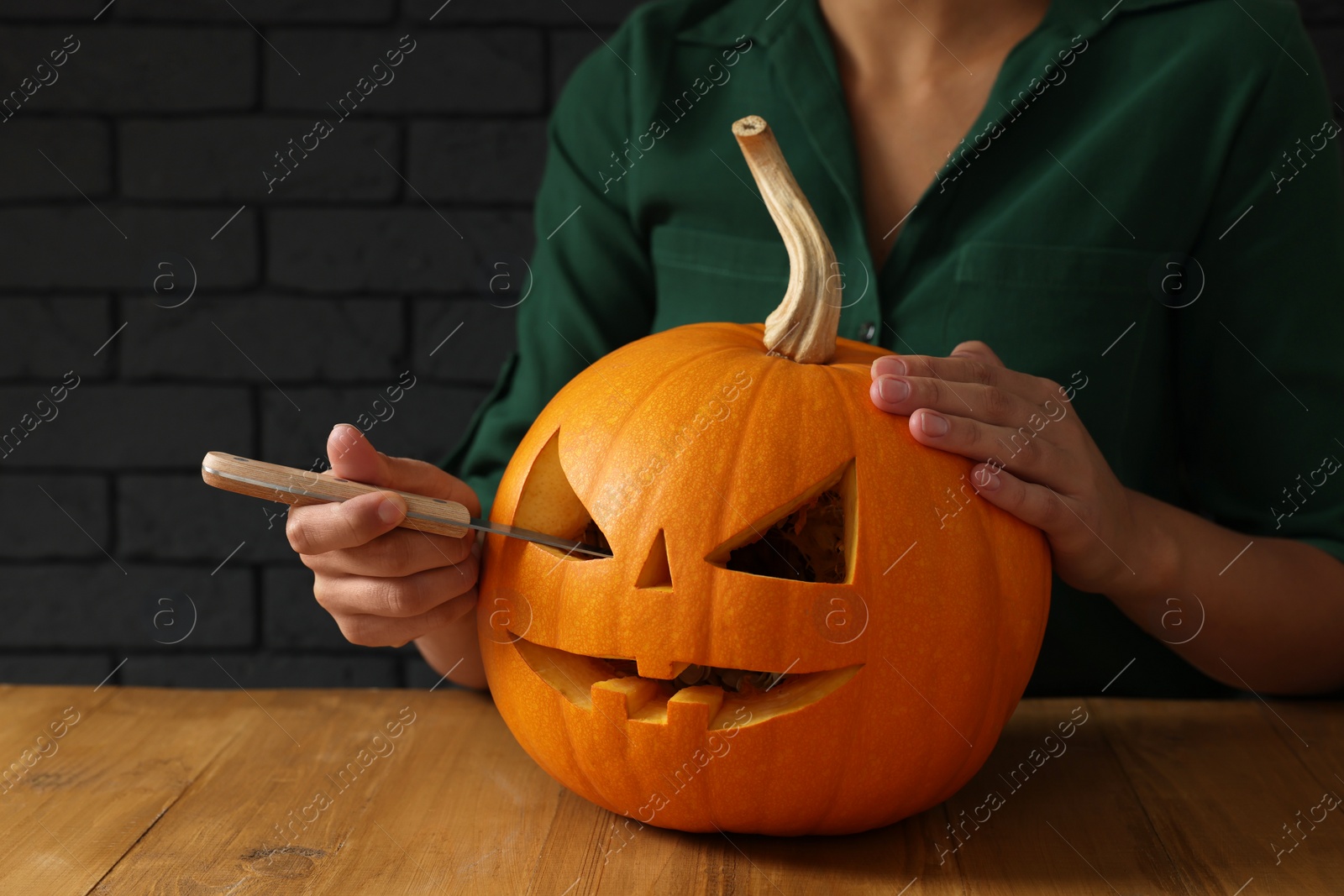 Photo of Woman carving pumpkin at wooden table, closeup. Halloween celebration