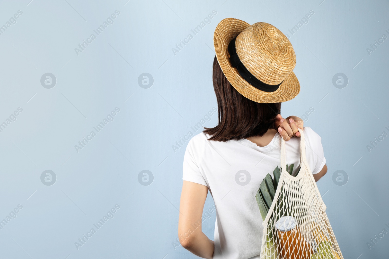 Photo of Woman holding mesh bag with fresh vegetables on grey background, space for text