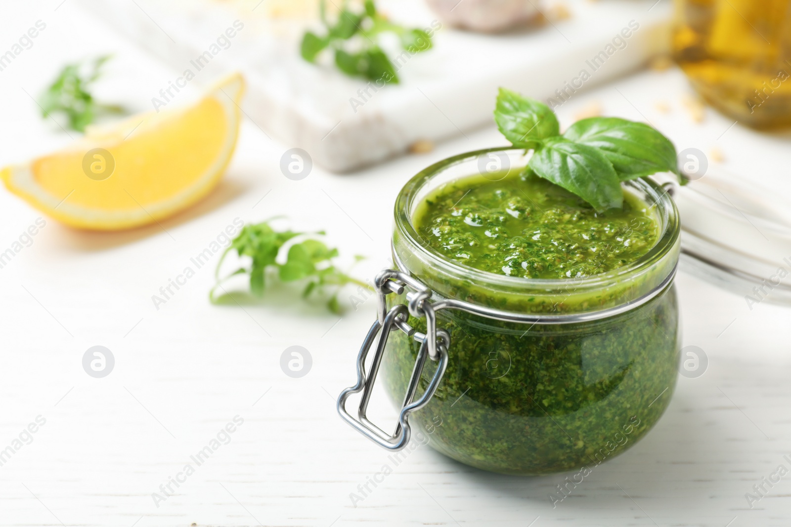 Photo of Homemade basil pesto sauce in glass jar on table