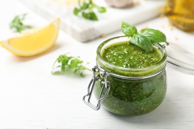 Homemade basil pesto sauce in glass jar on table