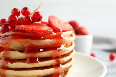 Delicious pancakes with fresh berries and syrup on table, closeup