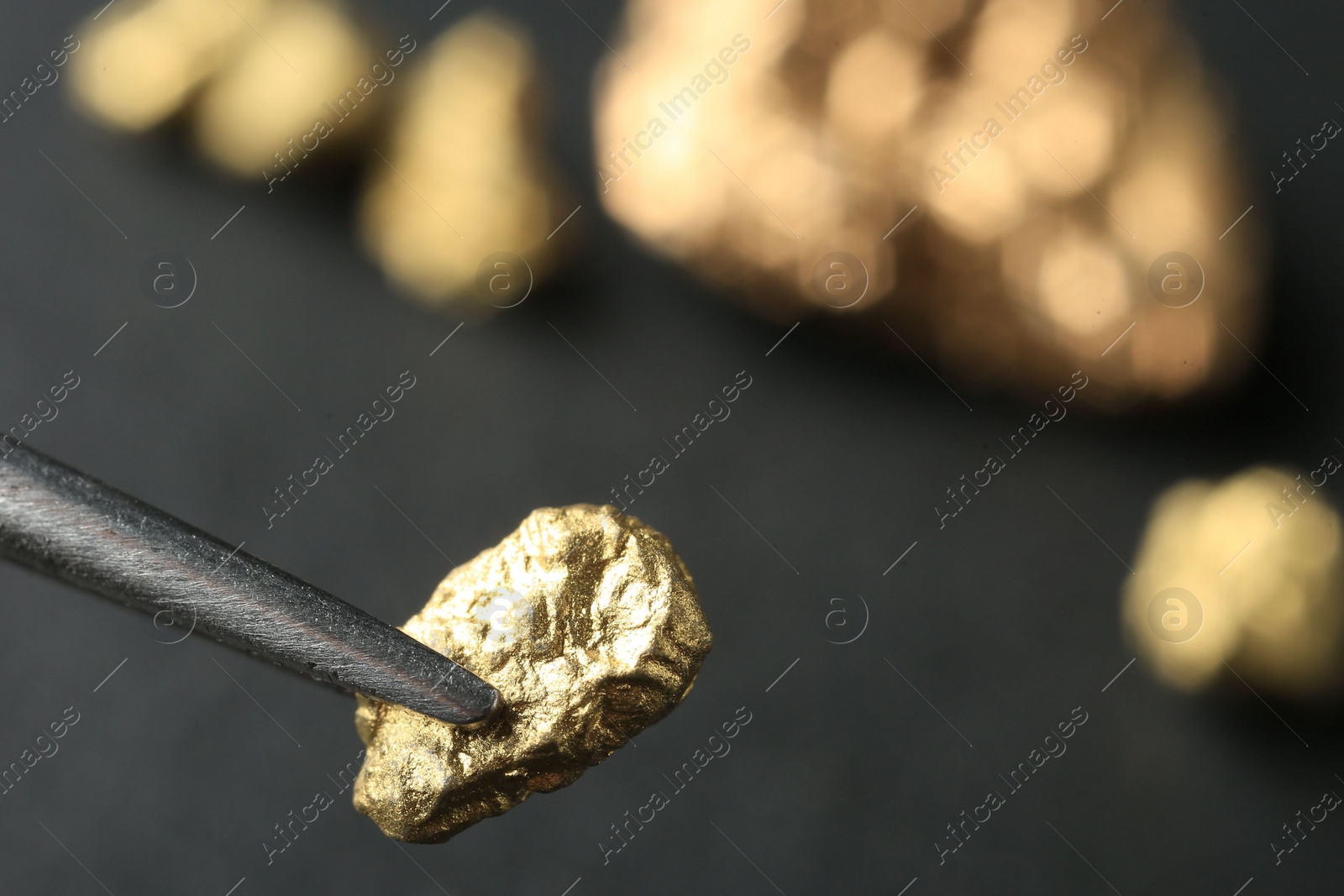 Photo of Tweezer with shiny gold nugget on blurred background, closeup. Space for text